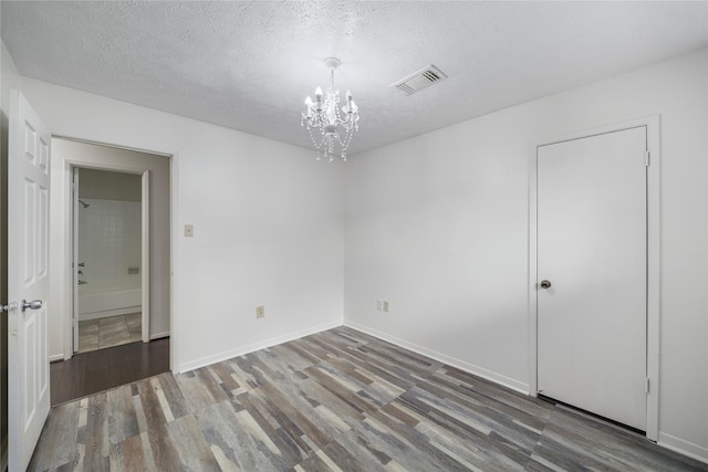 unfurnished bedroom with visible vents, a textured ceiling, an inviting chandelier, and wood finished floors