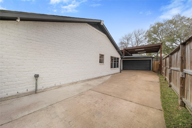 view of home's exterior featuring driveway, fence, an outdoor structure, and brick siding