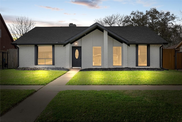 view of front facade featuring a shingled roof, brick siding, fence, and a front lawn