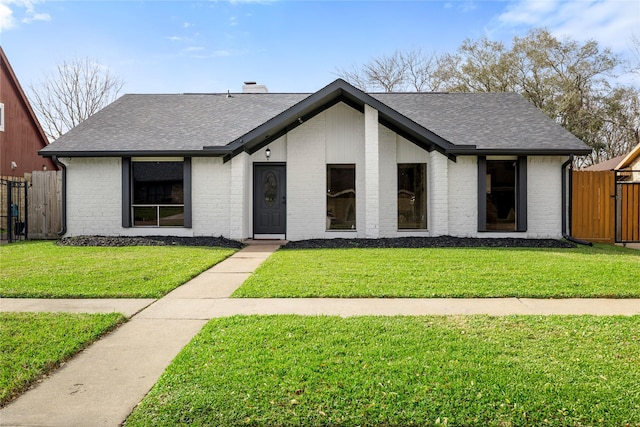 mid-century inspired home with brick siding, fence, a front lawn, and roof with shingles