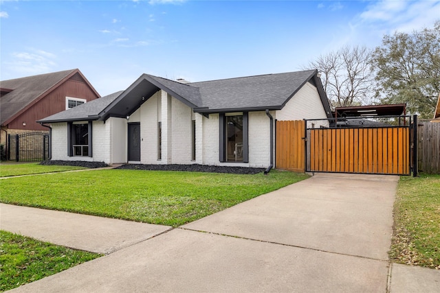 view of front of house featuring a shingled roof, a gate, a front lawn, and brick siding