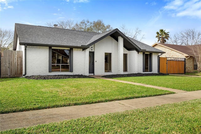 mid-century modern home with a shingled roof, brick siding, and fence