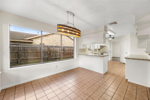 kitchen featuring light tile patterned floors, visible vents, a peninsula, a textured ceiling, and backsplash