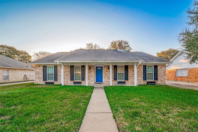 ranch-style home with roof with shingles, a front lawn, a chimney, and brick siding