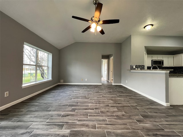 unfurnished living room with lofted ceiling, wood tiled floor, baseboards, and ceiling fan