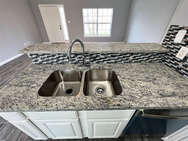 room details with light stone counters, decorative backsplash, white cabinetry, a sink, and baseboards