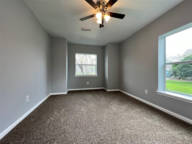 unfurnished room with a ceiling fan, visible vents, dark carpet, and baseboards