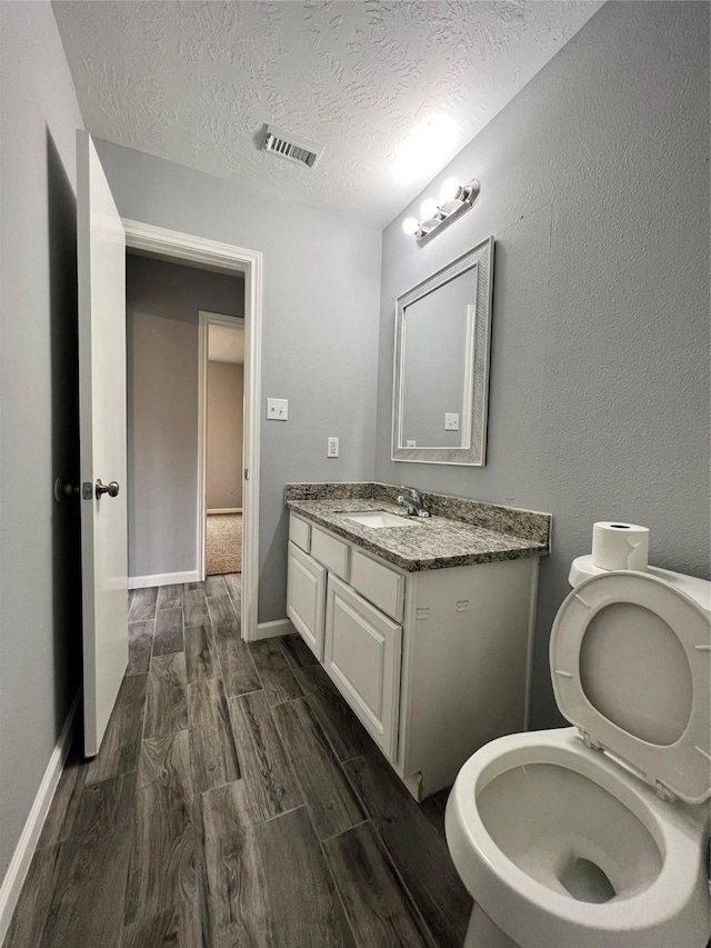 bathroom featuring a textured ceiling, wood finished floors, vanity, visible vents, and baseboards