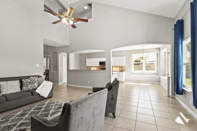 living room featuring baseboards, light tile patterned floors, ceiling fan with notable chandelier, arched walkways, and high vaulted ceiling