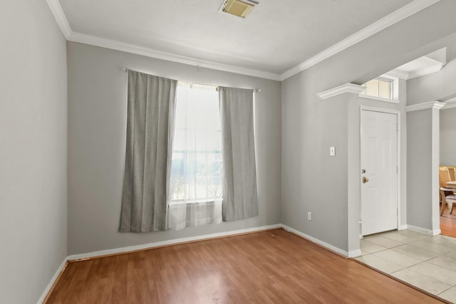 empty room featuring decorative columns, visible vents, wood finished floors, and ornamental molding