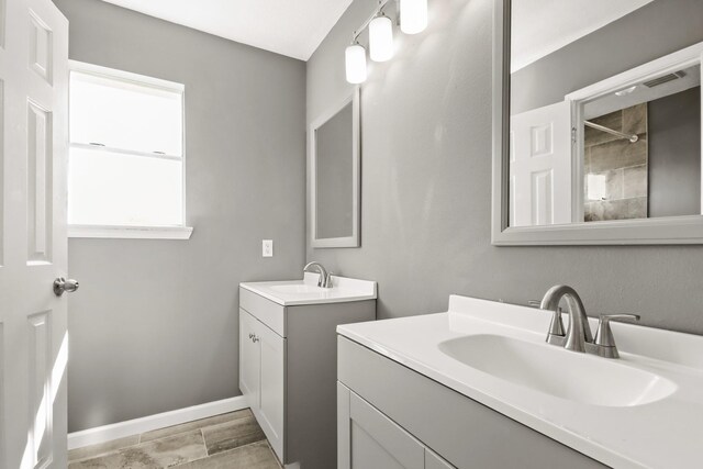 full bath featuring a sink, visible vents, baseboards, and two vanities