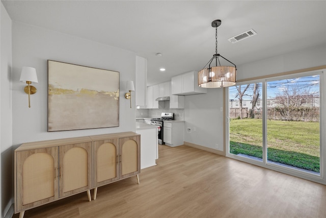 kitchen with visible vents, stainless steel range with gas cooktop, light wood finished floors, light countertops, and tasteful backsplash