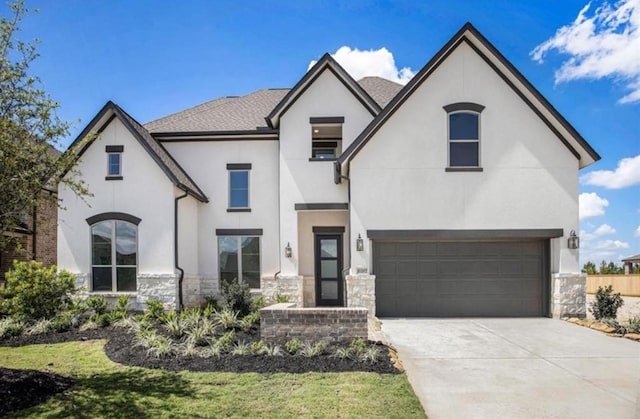 french country inspired facade featuring stone siding, an attached garage, concrete driveway, and stucco siding