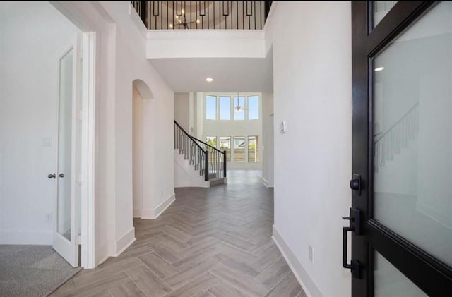 entryway featuring arched walkways, recessed lighting, a towering ceiling, baseboards, and stairs