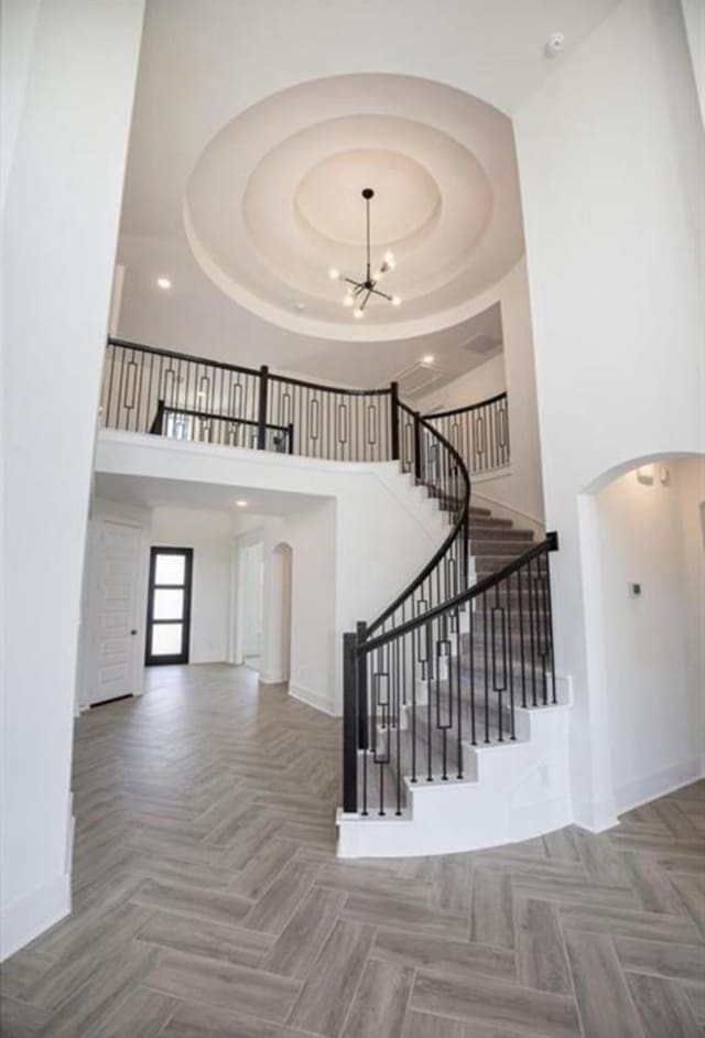 stairway with baseboards, arched walkways, a high ceiling, a tray ceiling, and a notable chandelier