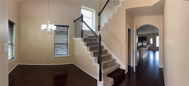 stairs featuring baseboards, arched walkways, a towering ceiling, wood finished floors, and an inviting chandelier