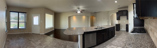 kitchen with arched walkways, a ceiling fan, light stone counters, stainless steel appliances, and a sink