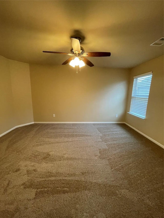 spare room with a ceiling fan, dark carpet, visible vents, and baseboards