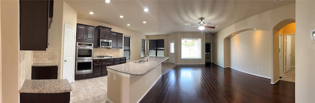 kitchen featuring dark brown cabinetry, decorative backsplash, light stone countertops, stainless steel appliances, and recessed lighting