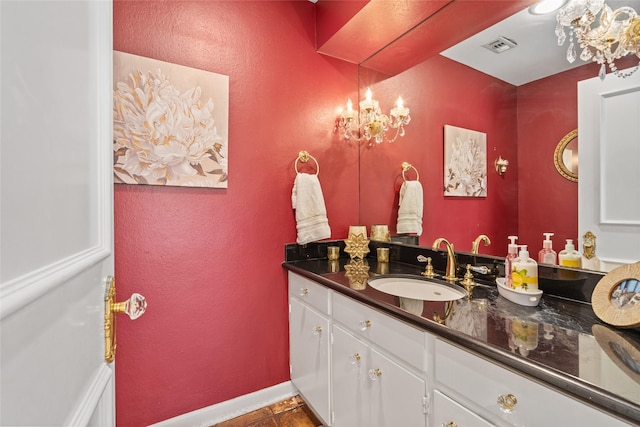 bathroom featuring a textured wall, visible vents, baseboards, vanity, and an inviting chandelier