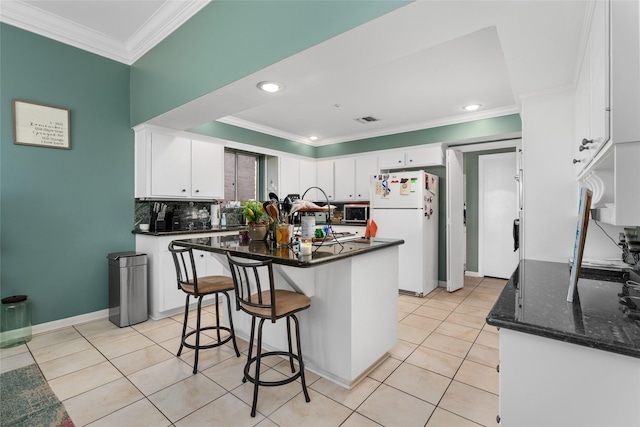 kitchen featuring light tile patterned flooring, white cabinets, freestanding refrigerator, stainless steel microwave, and crown molding