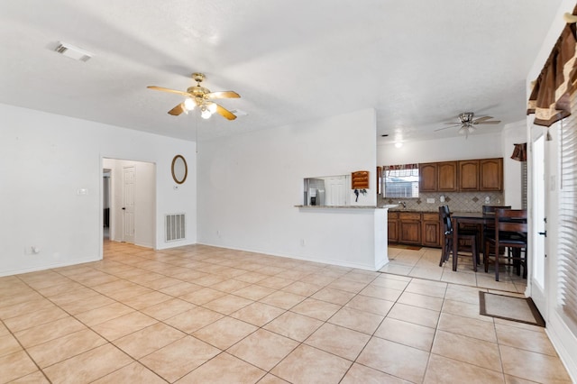 living room with light tile patterned flooring, a ceiling fan, visible vents, and baseboards