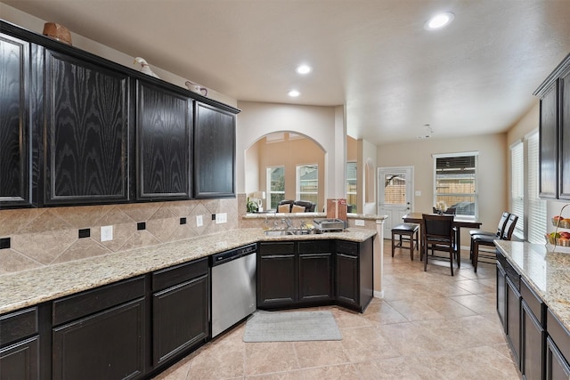 kitchen featuring light stone counters, a sink, decorative backsplash, dishwasher, and dark cabinets