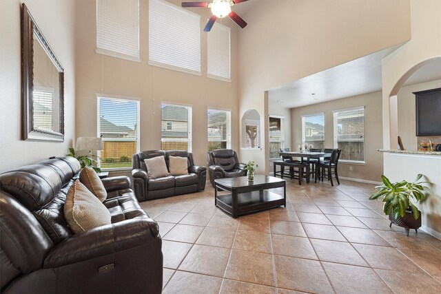 living room featuring light tile patterned flooring, a ceiling fan, a high ceiling, and baseboards