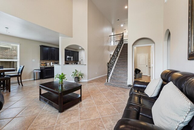 living room with light tile patterned floors, baseboards, arched walkways, and stairs