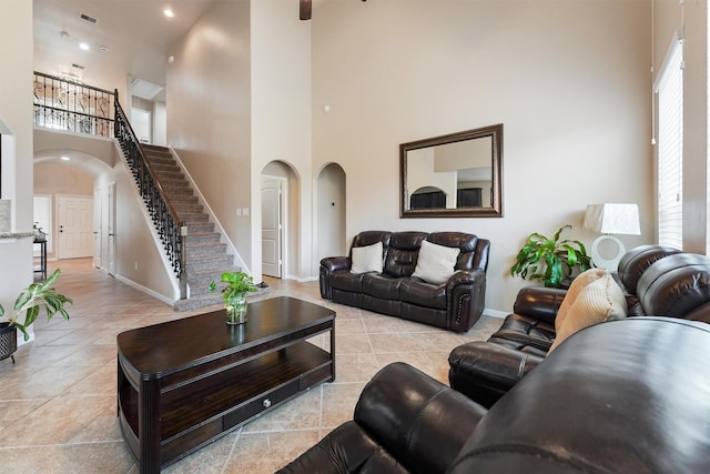 living room with light tile patterned floors, visible vents, arched walkways, and a towering ceiling