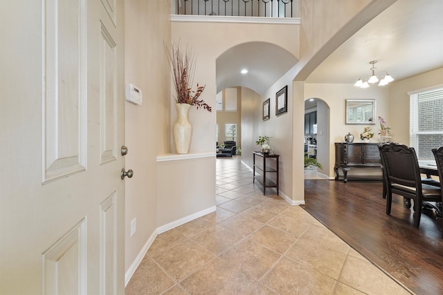 entrance foyer with a notable chandelier, arched walkways, a high ceiling, tile patterned flooring, and baseboards