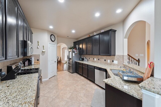 kitchen with light stone counters, recessed lighting, arched walkways, stainless steel appliances, and a sink