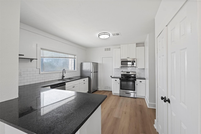 kitchen with a sink, tasteful backsplash, appliances with stainless steel finishes, a peninsula, and white cabinets