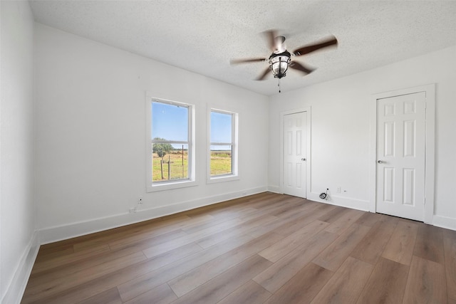 unfurnished room with ceiling fan, a textured ceiling, baseboards, and wood finished floors