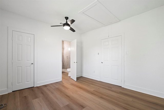 unfurnished bedroom featuring ensuite bath, attic access, baseboards, and wood finished floors