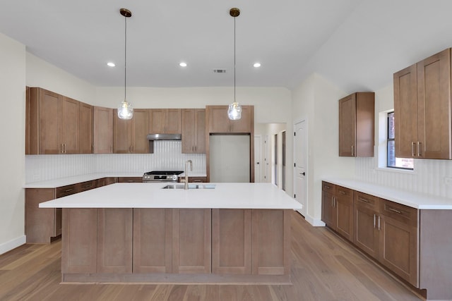 kitchen with decorative backsplash, a sink, an island with sink, stainless steel gas range, and under cabinet range hood