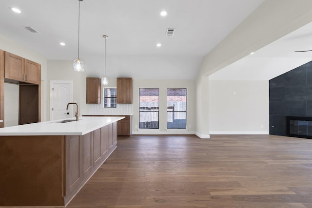 kitchen featuring visible vents, brown cabinetry, a tiled fireplace, dark wood-style floors, and a sink