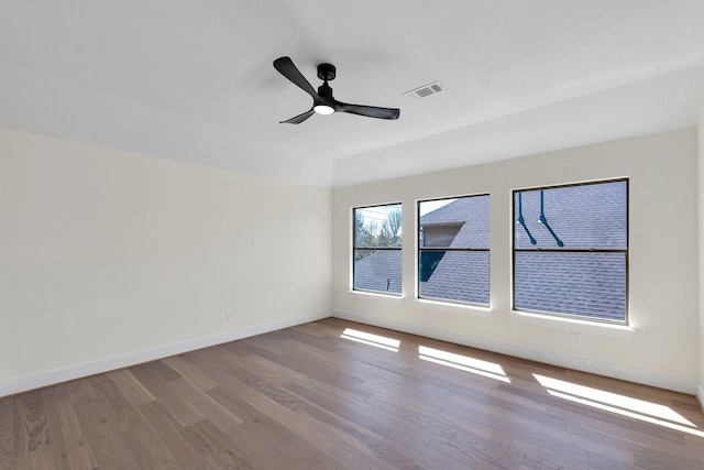 spare room featuring a ceiling fan, visible vents, baseboards, and wood finished floors