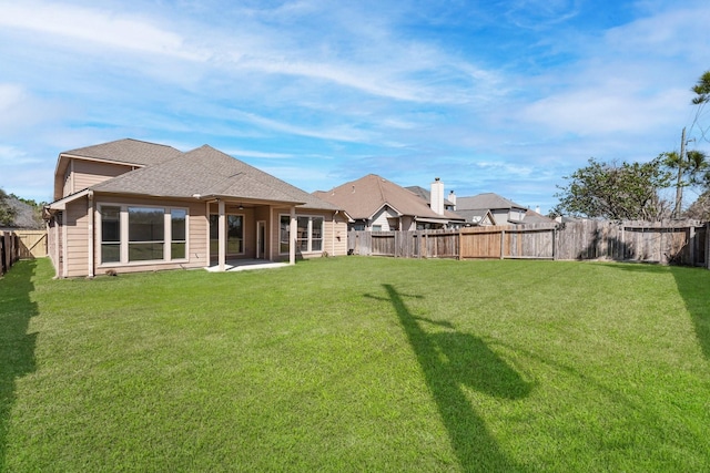 back of house with a shingled roof, a fenced backyard, a lawn, and a patio