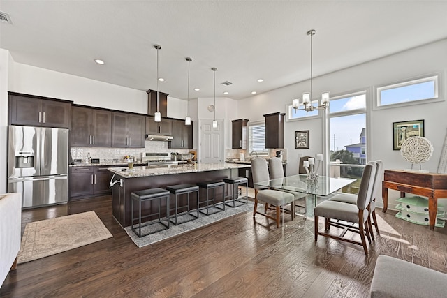 kitchen with dark wood-type flooring, under cabinet range hood, stainless steel fridge, range, and dark brown cabinets