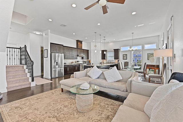 living room featuring baseboards, recessed lighting, dark wood-style flooring, stairs, and ceiling fan with notable chandelier