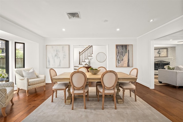 dining space featuring visible vents, a fireplace, crown molding, and wood finished floors