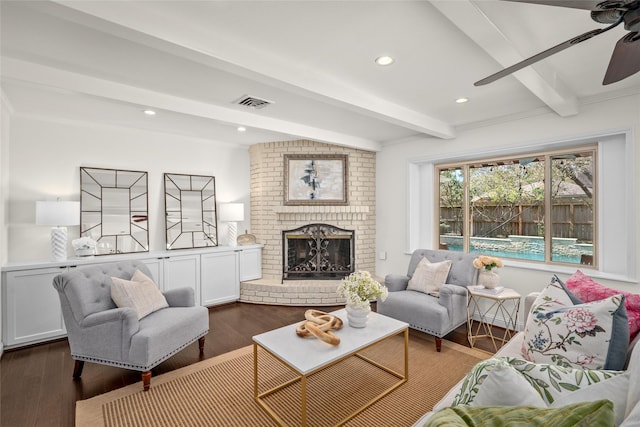 living area featuring beam ceiling, a brick fireplace, visible vents, and dark wood-style flooring