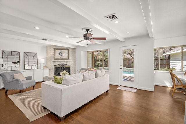 living room featuring beam ceiling, a fireplace, visible vents, and dark wood-type flooring