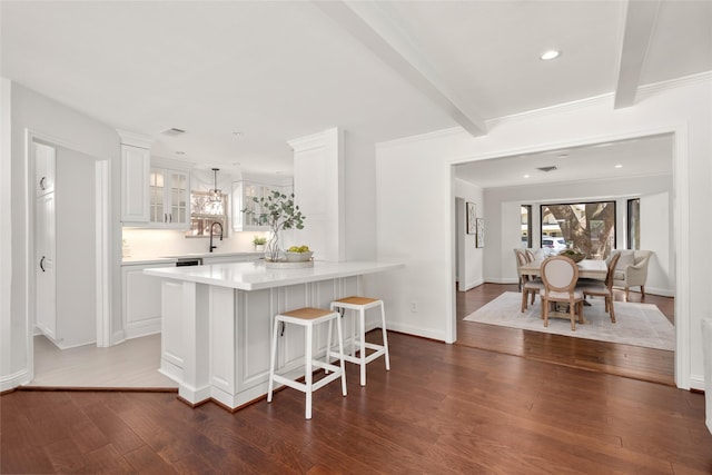 kitchen with beam ceiling, a kitchen breakfast bar, white cabinets, light countertops, and glass insert cabinets