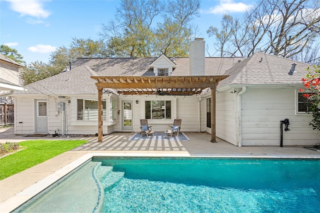 back of house featuring a patio, an outdoor pool, a pergola, a chimney, and a shingled roof