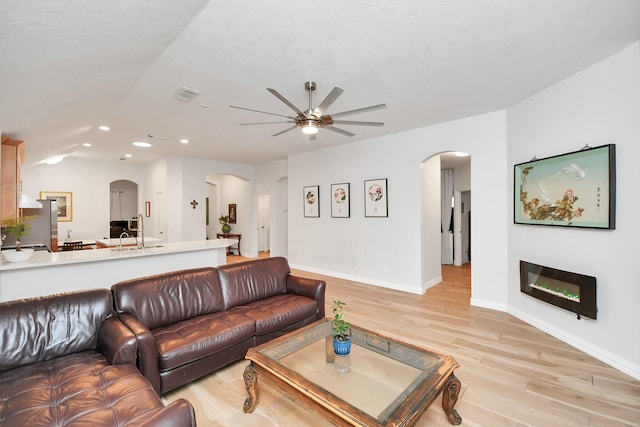 living area with arched walkways, a ceiling fan, light wood-style flooring, and baseboards