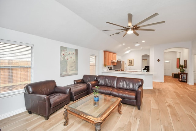 living area featuring arched walkways, ceiling fan, lofted ceiling, light wood-style flooring, and baseboards