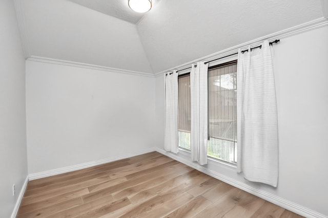 spare room featuring vaulted ceiling, plenty of natural light, light wood-style flooring, and baseboards