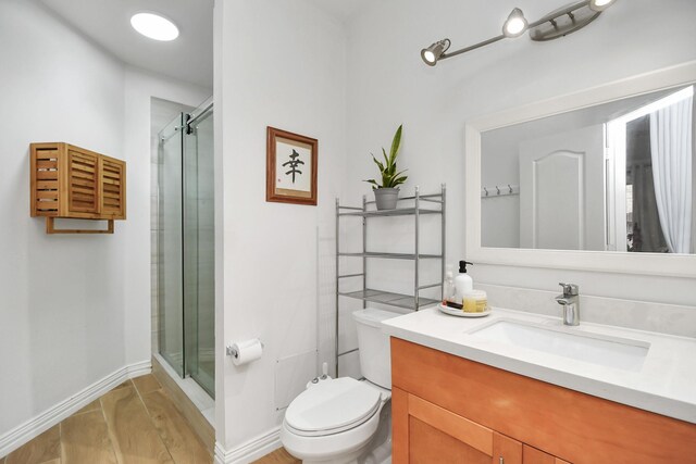 full bathroom with toilet, a stall shower, baseboards, and vanity